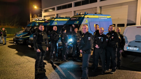 Groupe de 10 gendarmes de face dans la nuit. Ils se trouvent devant 3 camions d'intervention.