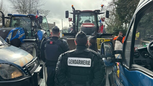 Deux gendarmes mobiles de dos fond face aux tracteurs des agriculteurs.