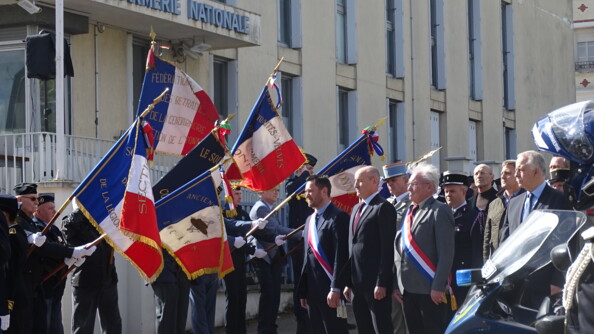 Motocycliste de la gendarmerie au premier plan. Au second plan, les autorités civiles et militaires passent en revue les portes-drapeaux.