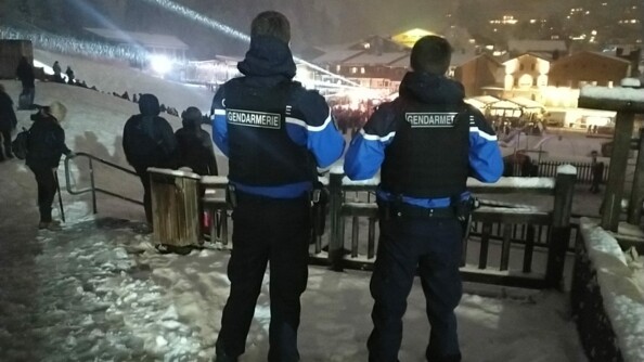 Dans une station des Alpes, deux gendarmes départementaux, les pieds dans la neige, surveillent une fête qui se déroule en contrebas.