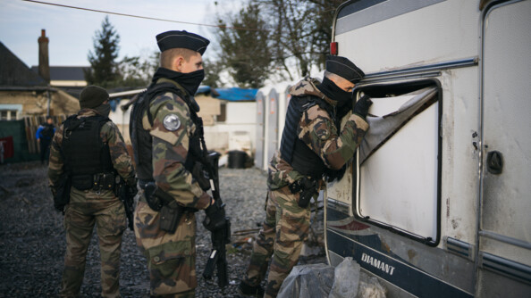 Trois gendarmes dans une décharge, dont un qui regarde à l'intérieur d'une caravane.