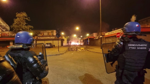Des militaires du PSIG SABRE avec leurs protections et leurs boucliers progressent dans une rue où des barricades ont été enflammées.