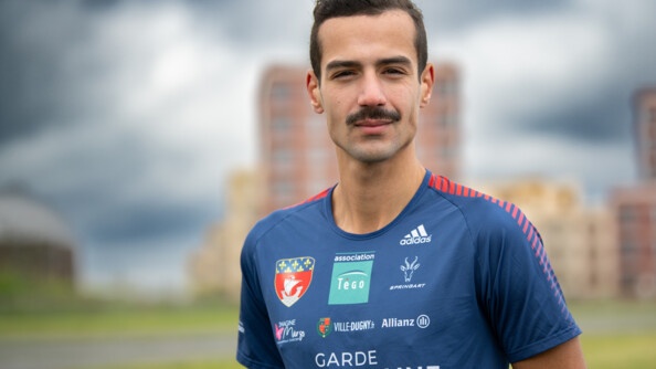 Nous voyons un portrait de Mehdi Frère, souriant, sur une piste d'athlétisme à Dugny, il fait un temps gris