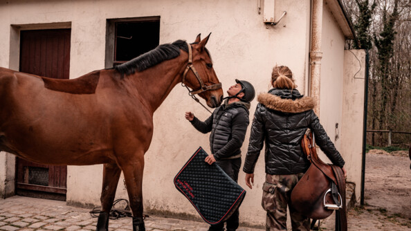 Nicolas, participant au stage Cent'Or, au centre, tapis de la Garde républicaine en main, mime un baiser avec son cheval, à gauche, sous le regard de son accompagnante, à droite, qui tient la selle contre sa hanche.