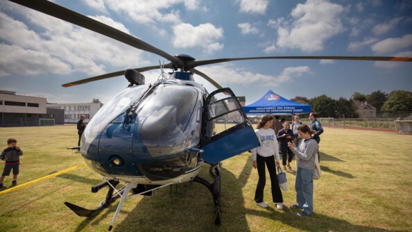 Un hélicoptère des forces aériennes au sol, sur un terrain du football, avec plusieurs visiteurs autour.