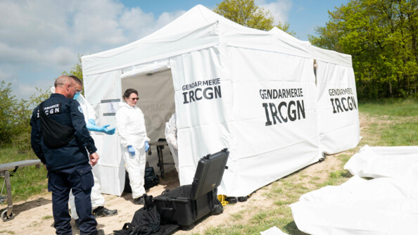 Dans une clairière, des gendarmes de l'IRCGN prépare le matériel pour analyser les corps retrouver dans le charnier. Ils sont à côté d'une tente de l'IRCGN.
