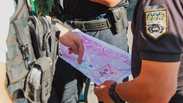 Trois gendarmes en cercle dont on ne voit que les mains, étudient ensemble une carte. L'un deux pointe un secteur sur la carte.