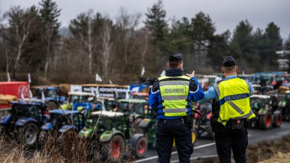 Deux gendarmes avec un gilet de sécurité et en extérieur, regardent de dos les tracteurs.