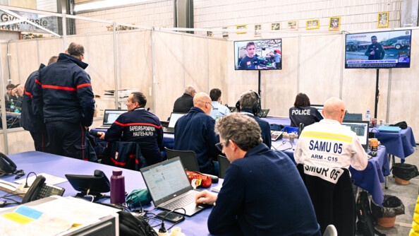 Dans une salle, des pompiers, des gendarmes, des personnels de la préfecture et d'autres acteurs de l'état, travaillent à la sécurisation de l'événement.