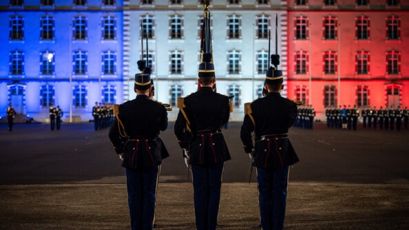 La garde au drapeau de l'EOGN, de dos, devant les OGR alignés devant l'etat-major de l'école illuminé de bleu blanc rouge