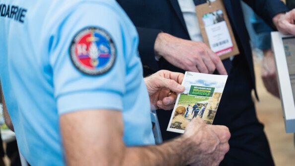 Un gendarme tenant dans sa main un flyer sur la sécurisation de l'exploitation agricole.