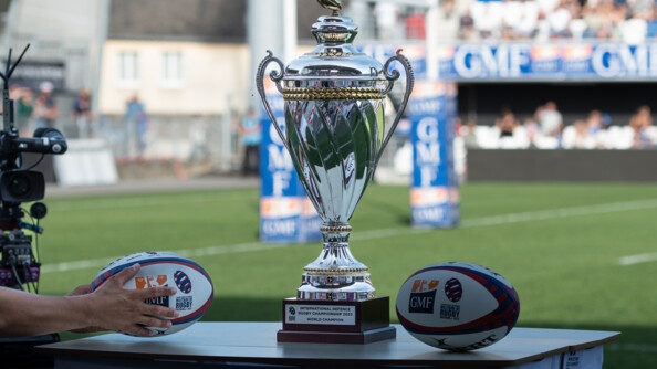 Trophée de la coupe du Monde militaire entouré de deux ballons de rugby