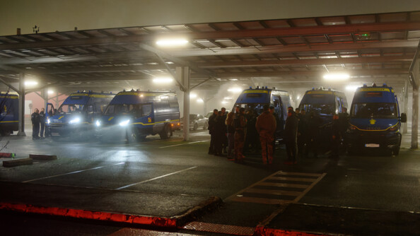 Une vingtaine de gendarmes sont regroupés dans un parking. Il fait nuit. Ils se trouvent devant 6 camions de gendarmerie.
