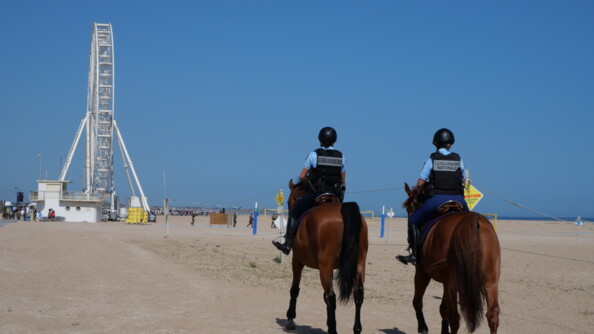 Deux gendarmes à cheval sur la plage qui s'avancent vers une grande roue.