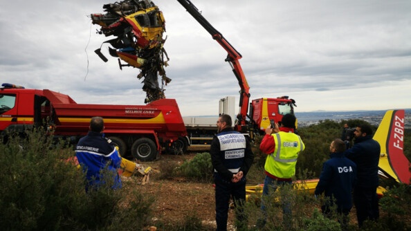 Carcasse d'un hélicoptère accidenté déplacé sur un camion grue de la sécurité civile, sous le regard d'enquêteurs de la gendarmerie des transports aériens et du Bureau enquêtes analyses.