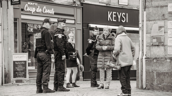 2 gendarmes et un policier discutant avec 3 femmes dans la rue. La photo est en noir et blanc.
