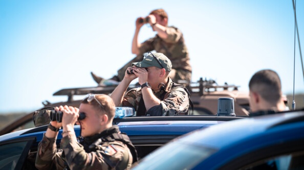 Trois militaires de l'armée de terre, postés côte à côte devant leur véhicule, regardent dans la même direction avec leurs jumelles