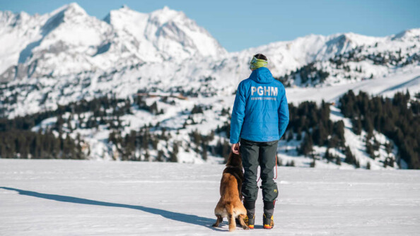 Un gendarme du PGHM regarde devant lui la station de ski. A ses côtés, son chien de recherche de personne.
