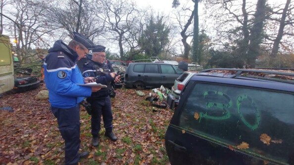 Deux gendarmes relevant les éléments au milieu d'un champ de véhicules épaves