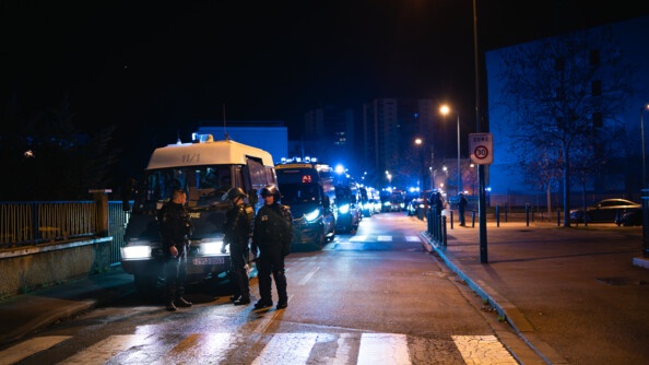 Dans la nuit, photo de trois gendarmes mobile dans la rue. En fond, de nombreux véhicules de gendarmerie sont allumés.