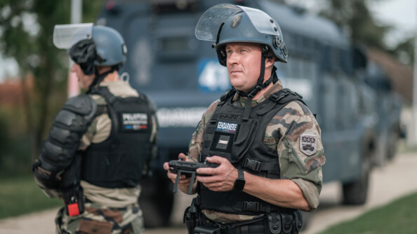 Droniste de la gendarmerie avec sa télécommande en main, devant un Centaure. A ses côtés, un gendarme mobile, en flou.