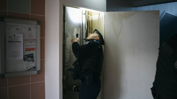 Un gendarme inspecte les parties communes d'un immeuble avec une lampe torche.