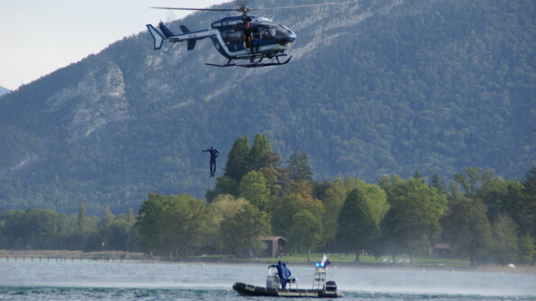 Le gendarme plongeur saute dans le lac depuis l'hélicoptère sous le regard attentif de deux de ses collègues.