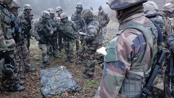 Briefing d'un groupe d'une quinzaine de gendarmes en tenue de combat. Ils sont dans la forêt et sous la pluie.