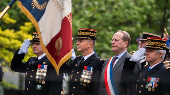 Trois militaires effectuent le salut devant le drapeau. Entre eux, se trouve un élu portant l'écharpe tricole sur la poitrine