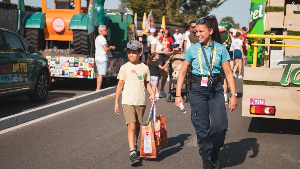 Agrandir l'image Le jeune Malo démabule dans la caravane du Tour de France à la recherche de goodies avec une gendarme.