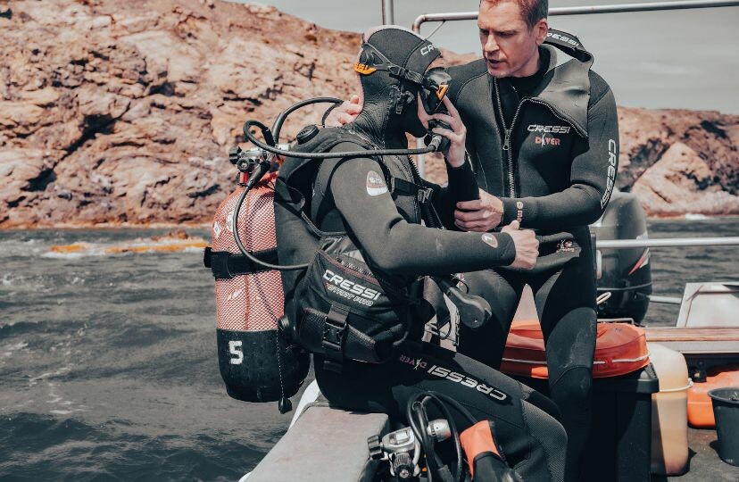 Une gendarme équiée d'une combinaison et d'une bouteille à oxygène s'apprête à plonger tandis qu'un moniteur lui donne des dernières instructions.