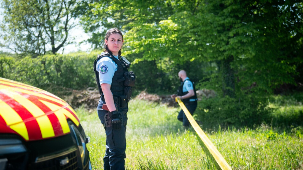 Une gendarme regarde à l'horizon au premier plan pendant qu'un gendarme déroule la rubalise en arrière plan.
