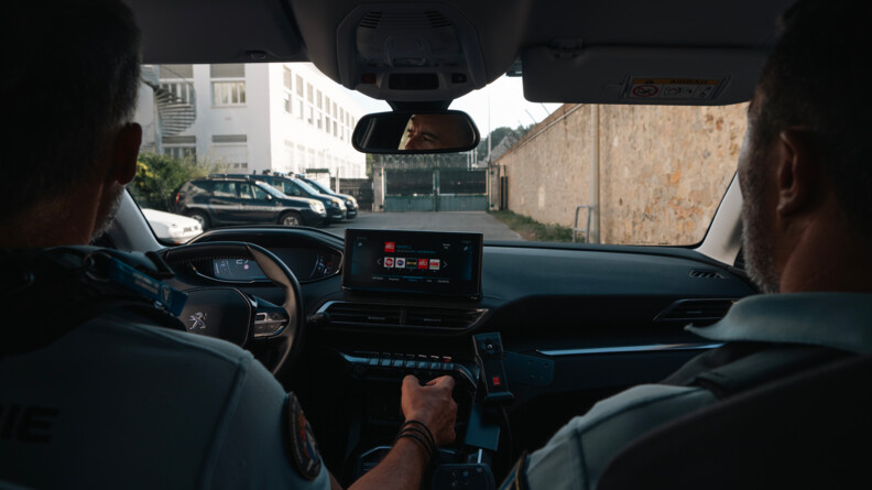 Dans une voiture, deux militaires de la GARM se dirige vers une barrière sécurisée.