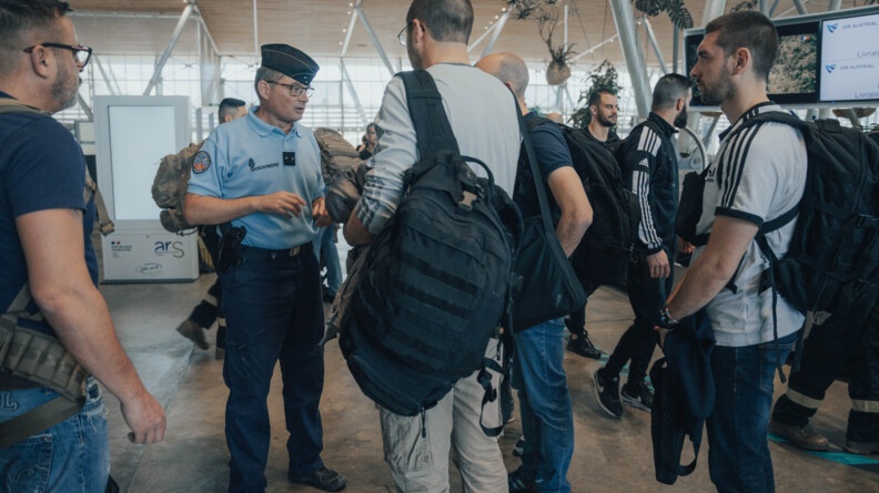 Le général Labrunye en tenue d'intervention, pantalon bleu foncé et polo bleu clair, calot sur la tête, de face, s'adressant à plusieurs hommes en civil que l'on voit de dos et de profil.