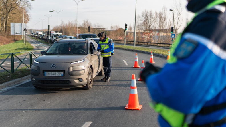 Sur une route retrécie par des plots oranges, un gendarme proède au contrôle d'un conducteur - vue au premier plan à droite, flou, d'un gendarme