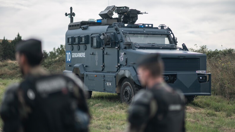 Agrandir l'image Deux gendarmes mobiles au premier plan en flou. A l'arrière plan le véhciule blindé Centaure sur un monticule en herbe.