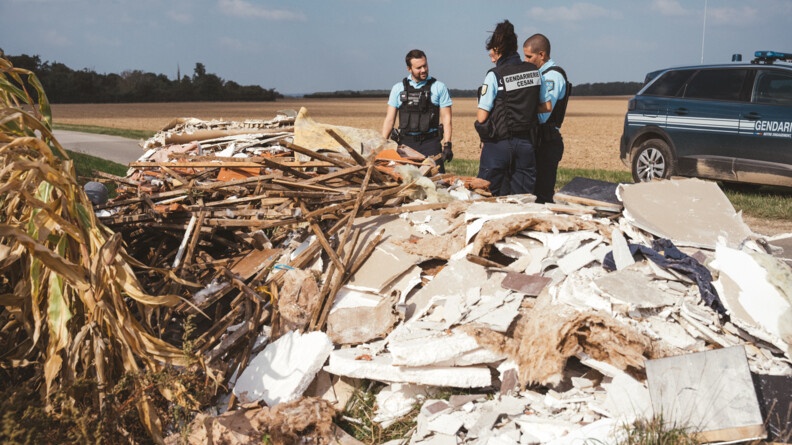 Trois gendarmes au bord d'un dépôt de déchets le long d'une route et d'un champ