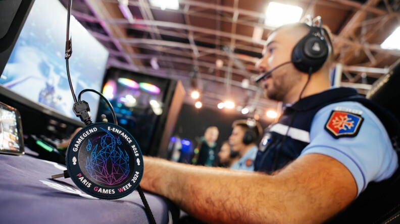 Zomm sur un écusson Gamegend Paris Games Week 2024 e-enfance 3018 - en flou un gendarme devant un ordinateur avec un casque