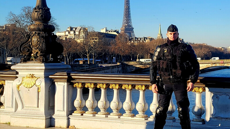 Agrandir l'image Un gendarme mobile debout devant la balustrade d'un pont de Paris. En arrière-plan, la Seine, Paris et la Tour Eiffel