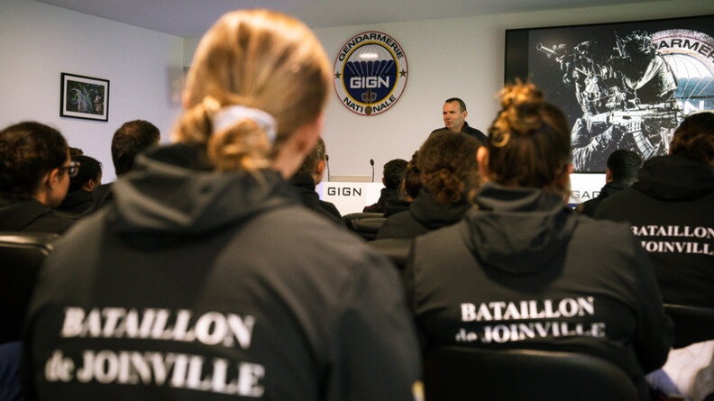 Des sportifs de dos au sweat noir floqué en blanc "bataillon de Joinville" écoute le chef du GIGN qui s'adresse à eux