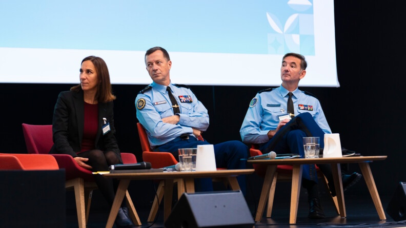 Photo de trois intervenants au colloque, assis sur des chaises rouges sur l'estrade d'un amphi.