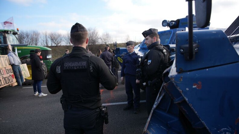 Trois gendarmes devant des véhicules blindés, regardent les agriclteurs et leur tracteur qui leur font face.