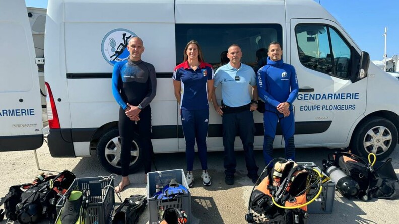 Agrandir l'image Charlotte Bonnet pose avec les gendarmes des brigades fluviale et nautique de Martigues, devant leur véhicule de gendarmerie, avec au premier plan l'équipement de plongée.