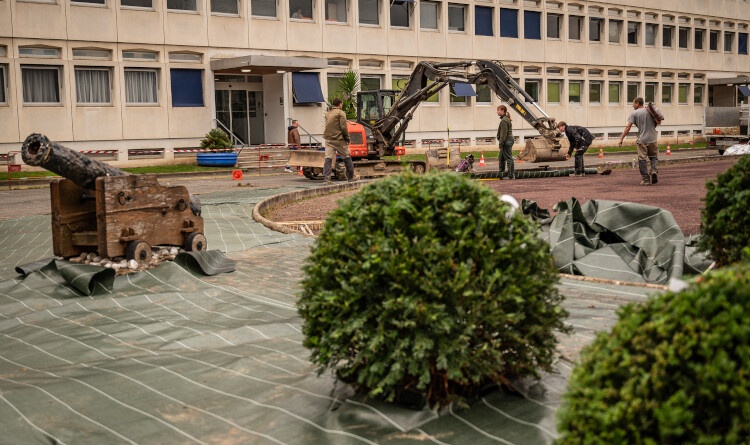 photo d'un grand b&acirc;timent en beton beige, devant lequel manoeuvre un engin de chantier. Des arbustes sont visibles en premier plan.