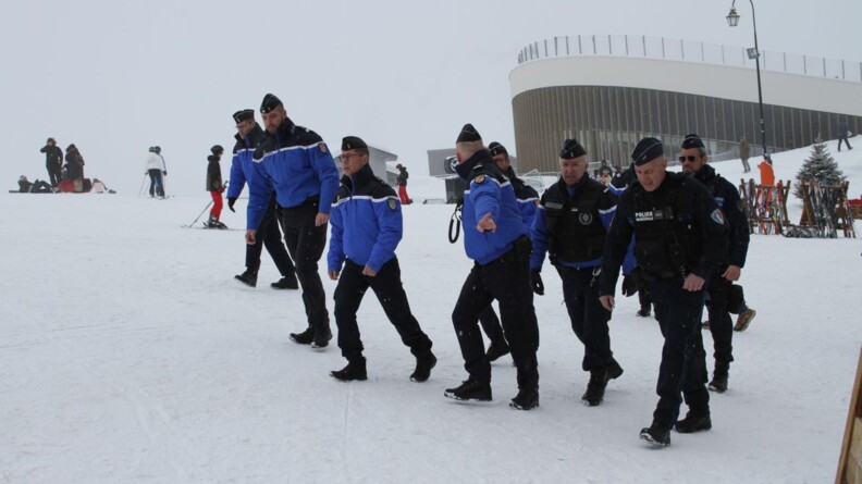 Agrandir l'image Des gendarmes, parmi lesquels le major général de la gendarmerie nationale, et des policiers municipaux, marchent sur la neige, au pied des pistes de ski, tandis que la neige tombe.