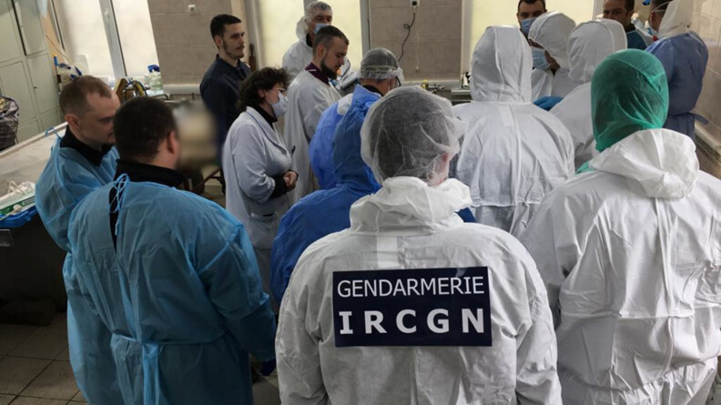 Agrandir l'image Un groupe de 16 personnes réunies dans une pièce carrelée. La plupart sont de dos. Elles portent des blouses bleues ou des combinaisons blanches et des charlottes ou une capuche sur la tête. Au première plan, l'une des personnes porte un scratch "GENDARMERIE IRCGN" en blanc sur fond bleu foncé dans le dos.
