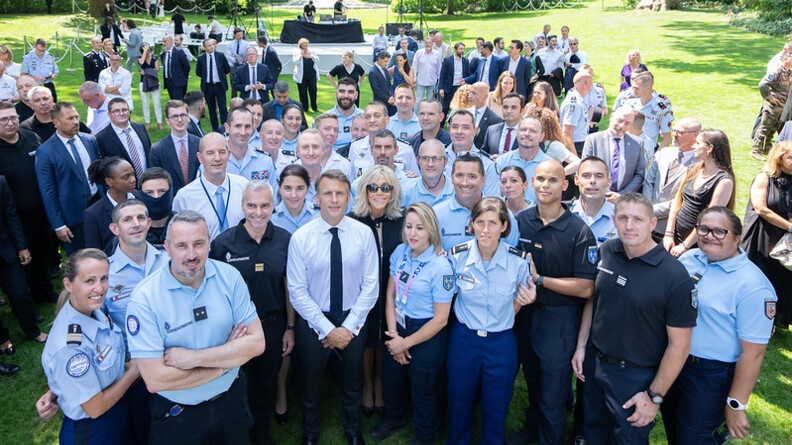 Le chef de l'Etat, Emmanuel Macron, et son épouse, posent au milieu d'un groupe de gendarmes en uniforme, dans les jardins du palais del'Elysée.