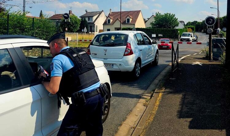 Un gendarme, vu de dos, dispense des conseils de pr&eacute;vention par la vitre du passager, &agrave; un conducteur arr&ecirc;t&eacute; derri&egrave;re un autre v&eacute;hicule, devant un passage &agrave; niveau (en arri&egrave;re-plan), dont la barri&egrave;re est baiss&eacute;e.