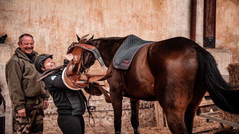A gauche de l'image, Pauline, participante du stage Cent'Or, et son accompagnant, en plein fou rire au moment de seller le cheval, à droite.