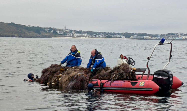 Agrandir l'image Deux gendarmes sur un Zodiac rouge, en train de remonter des filets. Dans le fond, le littoral.